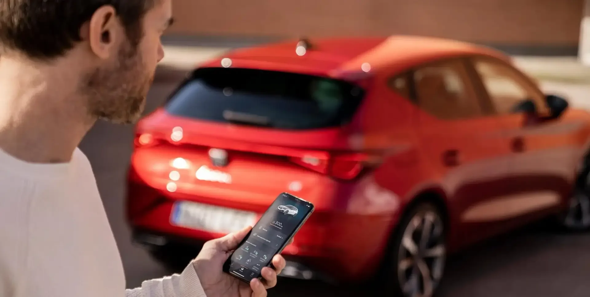 Mann bedient App SEAT Connect auf dem Handy, roter SEAT steht im Hintergrund