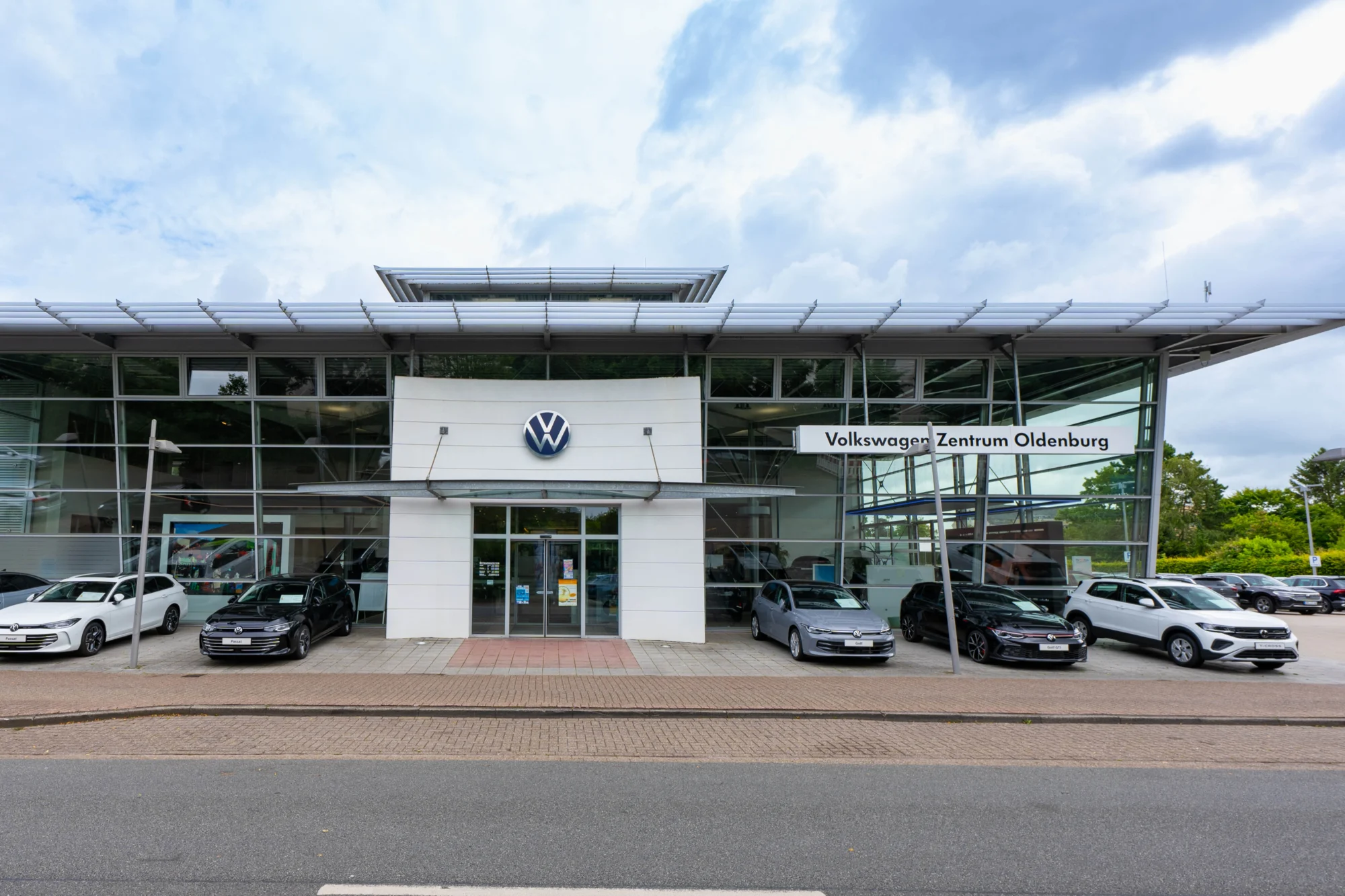 Volkswagenzentrum Oldenburg Ansicht Gebäude von vorne, rechts daneben Fahrzeuge auf dem Hof. Markenlogos oben rechts.